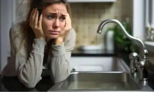 foto di una signora con le mani sul viso e l'espressione esasperata davanti al lavandino della cucina otturato